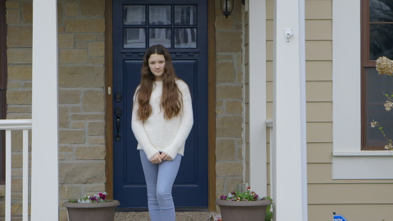 Girl standing on porch at home looks into camera, medium shot