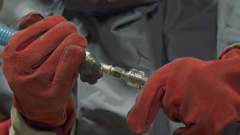 Worker-with-leather-gloves-connects-metal-pipes-in-workshop