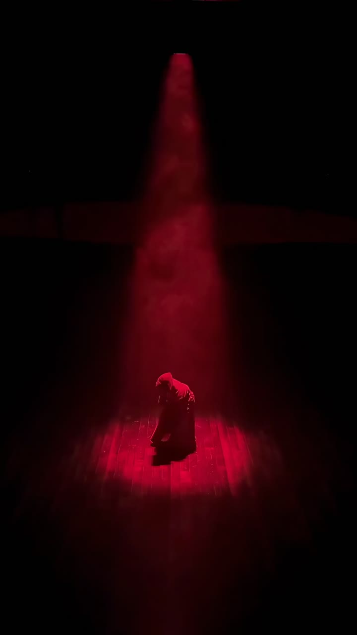 Dramatic video scene with a hooded figure in red spotlight, captured from a high angle