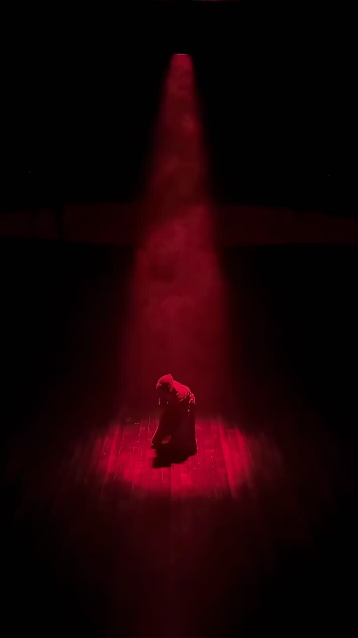 Dramatic video scene with a hooded figure in red spotlight, captured from a high angle