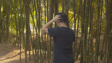 un hombre camina a través de un bosque de bambú rascándose la cabeza calva y cepillando la caspa