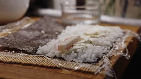 Female-preparing-sushi,-adding-crab-sticks-to-rice-on-makisu