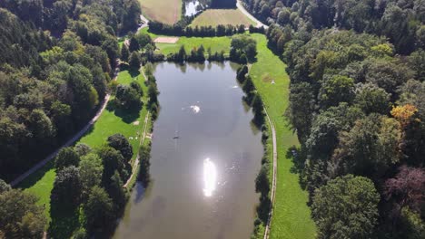 Aerial shot of a swimming lake surrounded by a green forest and green meadows during summer