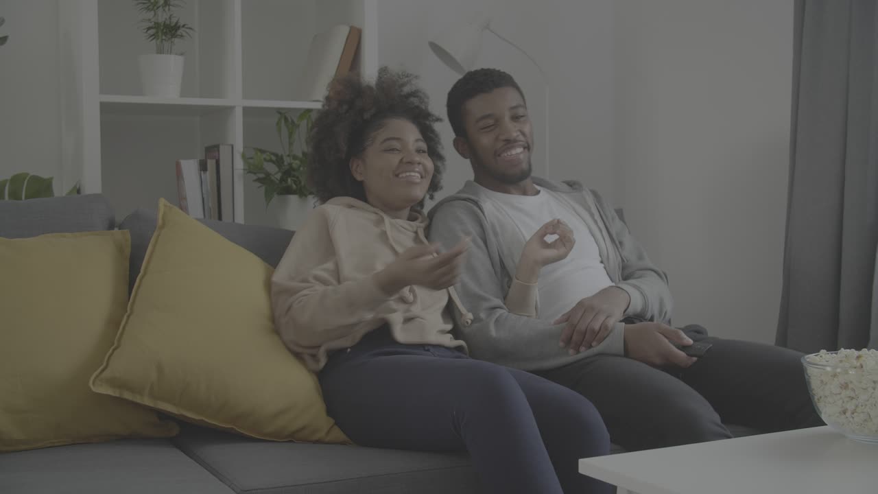 Young african american couple having fun while watching a movie on TV