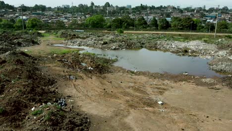 dirty dumping site with stagnant unhealthy water, rubbish and trash separated by highway and sad urban slums in background