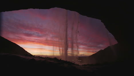 Toma-En-Cámara-Lenta-De-La-Cascada-De-Seljalandsfoss-Desde-El-Interior-De-Una-Cueva-Durante-La-Puesta-De-Sol.