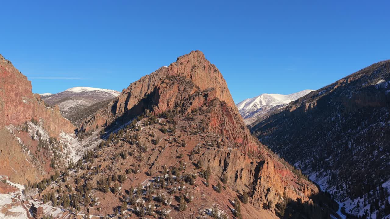 Una vista aerea cinematografica evidenzia una vetta montana affilata e prominente. La luce invernale nitida e le robuste texture rocciose definiscono l'immensa scala di questa cima montana ad alta quota.