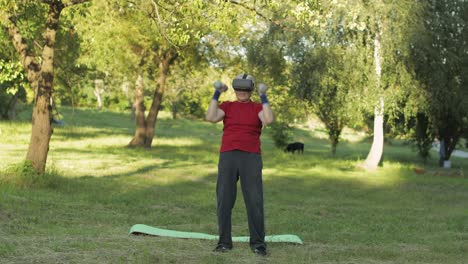 Senior-old-grandfather-man-in-VR-headset-helmet-making-fitness-exercises-with-dumbbells-outdoors