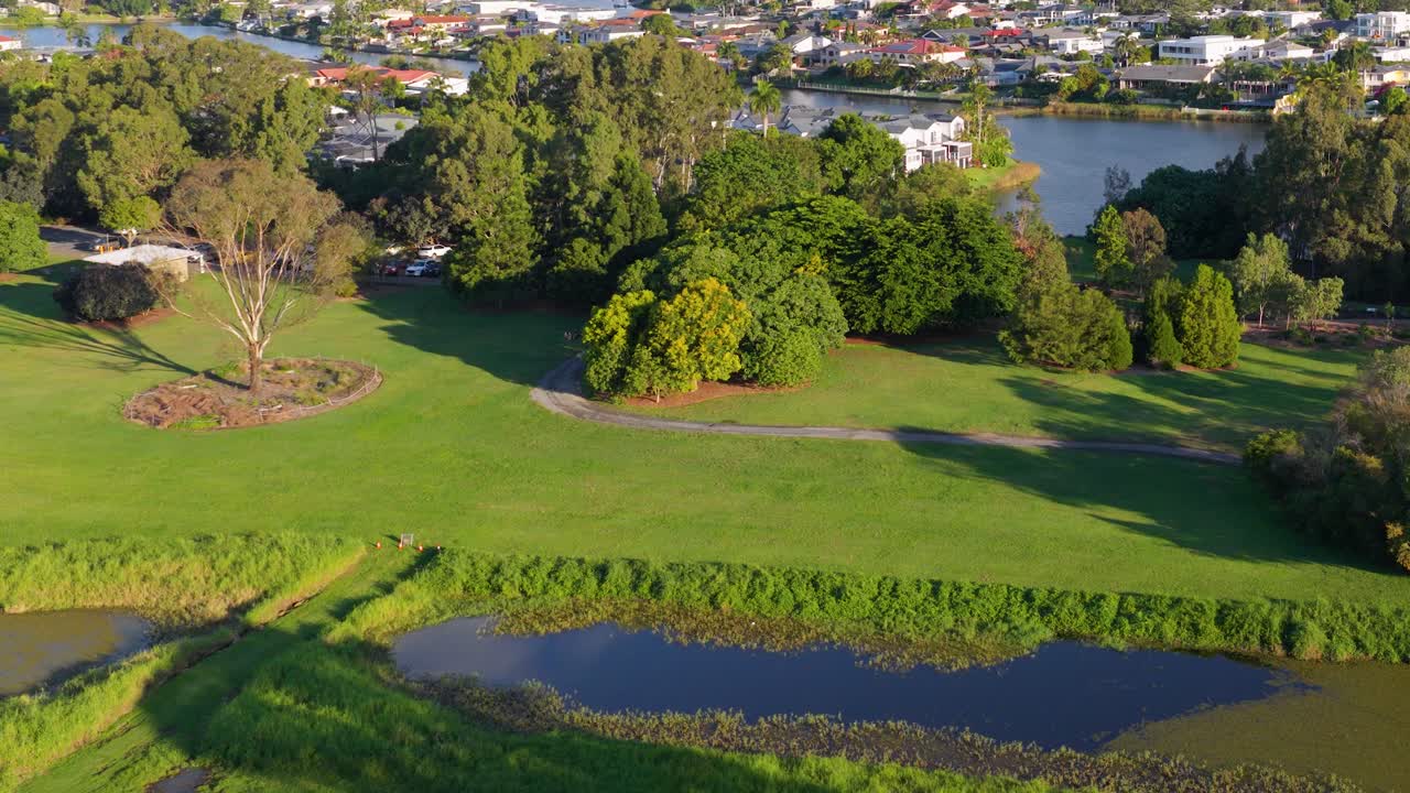 Drone footage captures lush greenery, river, and luxury homes in Gold Coast, Australia. Vibrant colors and smooth camera movement create a serene atmosphere