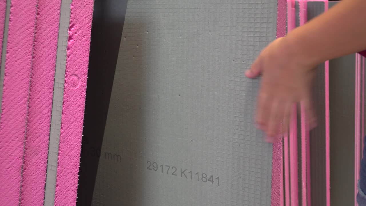 manos femeninas inspeccionando material rosa para el aislamiento del hogar en la ferretería