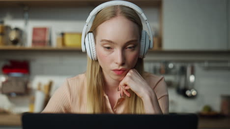 una chica independiente viendo un video de entrenamiento con auriculares sentada en la cocina de cerca.