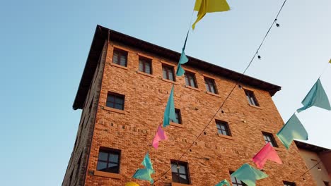 a building made of bricks: a bluesky as a background and fair flag buntings with lights hanging from wires sprang across