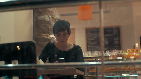 Young-woman-in-cafe-typing-message-on-mobile-with-happy-look