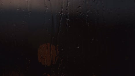 gotas de lluvia en la ventana con una luz redonda en la oscuridad. concepto. cerrar la superficie húmeda de vidrio con gotas de agua goteando hacia abajo y la luz tenue de la lámpara de la calle detrás de la ventana