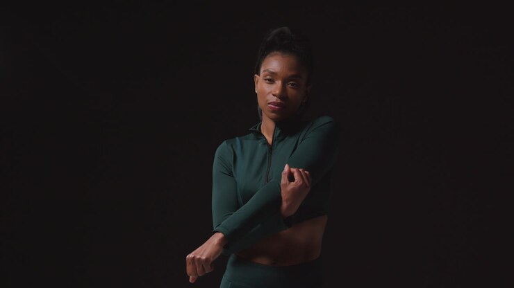 Portrait Of Determined Female Athlete Wearing Tracksuit Training Warming Up And Stretching Against Black Studio Background