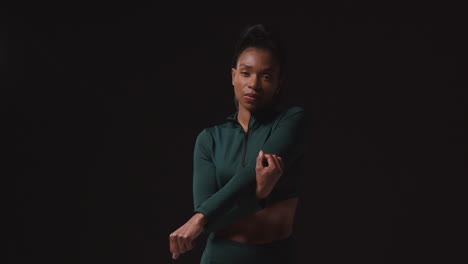 retrato de una atleta femenina decidida que lleva un traje de entrenamiento calentándose y estirándose contra un fondo de estudio negro