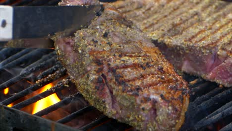 a pair of meat tongs turn a nearly cooked juicy rib eye steak on a grill and slides it a bit