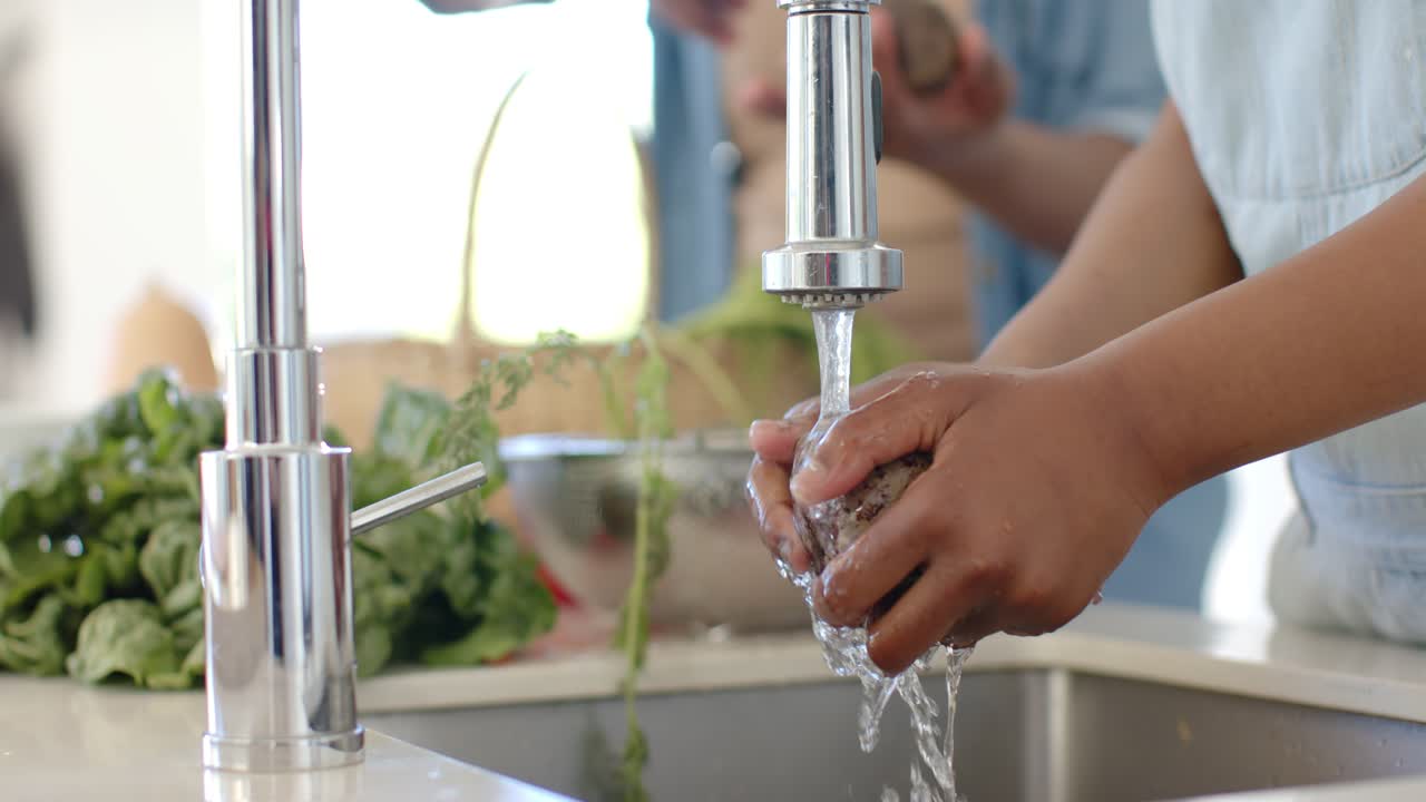 Faucet turning on is sending water while child's hands are scrubbing potato at sink for cooking