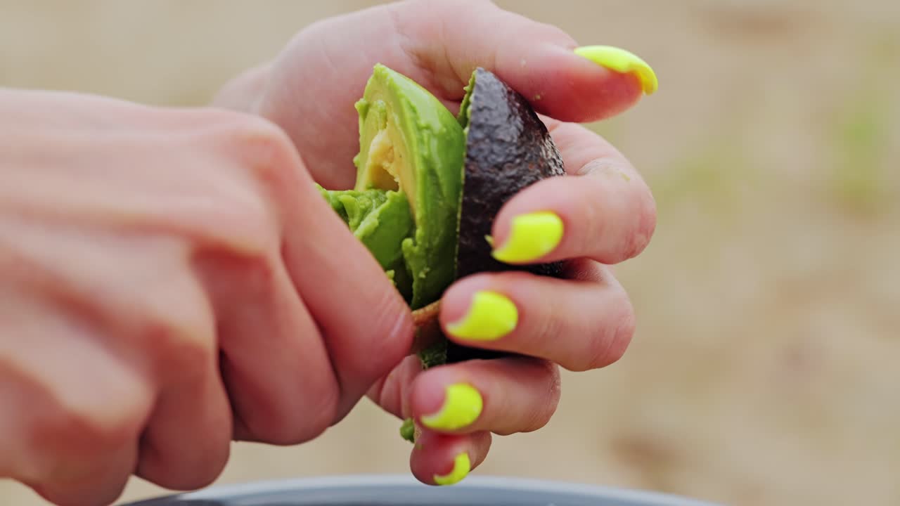 Biodegradable spoon scoops avocado flesh from peel in close-up forest shot