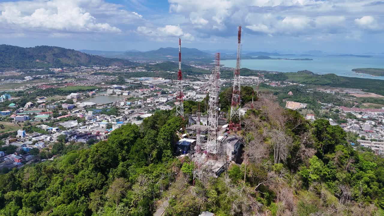 Drone footage captures telecommunication towers atop Monkey Hill in Phuket, Thailand, surrounded by lush greenery and urban landscape