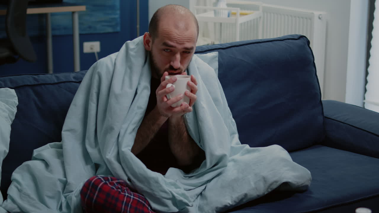 Man with cold shivering and drinking cup of tea