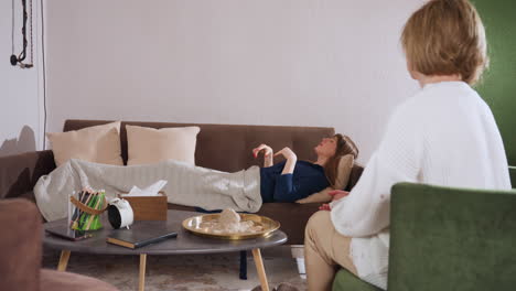 lady in blue gown relaxes on couch during therapy session, pulling soft blanket over herself while specialist observes nearby in peaceful setting with cozy decor and warm ambient lighting