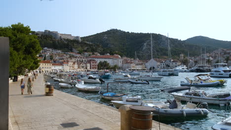 People-Walking-At-Promenade-With-Boats-Moored-At-Port-In-Hvar,-Croatia