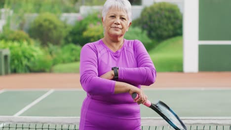 video de una feliz mujer mayor biracial sosteniendo una raqueta en una cancha de tenis