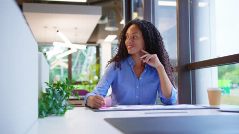 Mujer-De-Negocios-Sentada-En-Un-Escritorio-En-Una-Oficina-Abierta-Aprobando-O-Revisando-Pruebas-O-Diseños-De-Diseño.