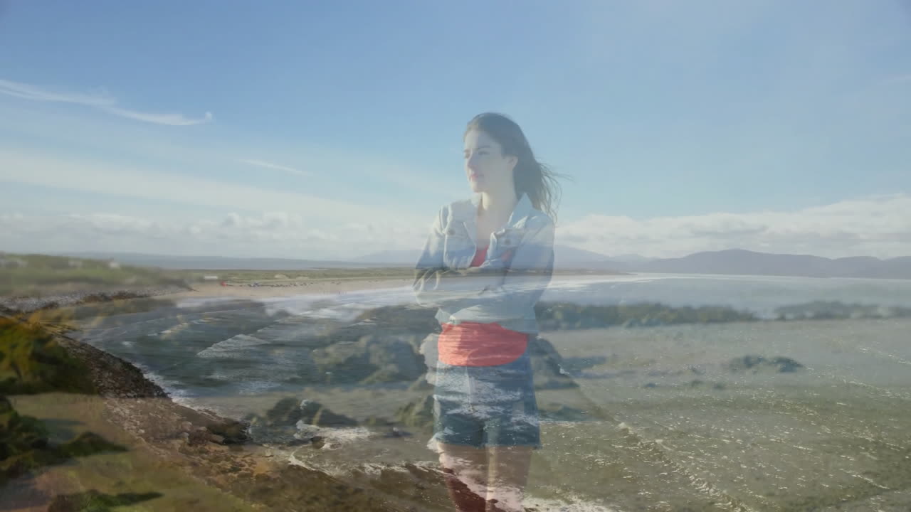 Standing on rocky beach, woman watching ocean waves under clear blue sky
