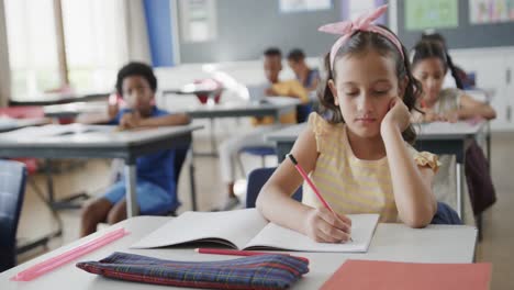 escolares diversos centrados en los escritorios aprendiendo y escribiendo en el aula en la escuela primaria