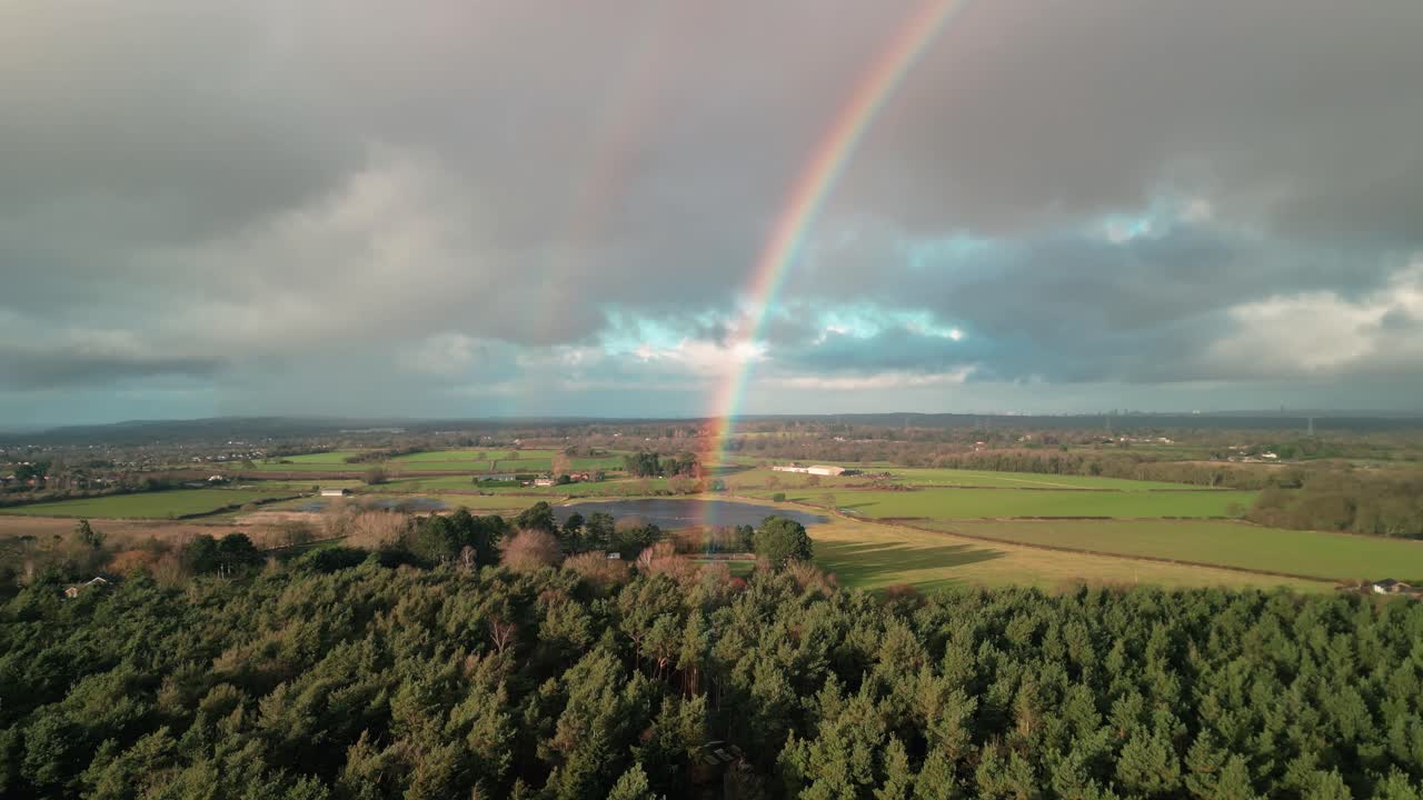 Wintertime sunny aerial drone flyover towards a beautiful double rainbow over a Cheshire pond, UK