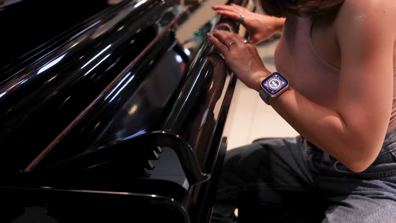 Woman in casual clothing opening grand piano lid in modern, well-lit indoor setting, close-up