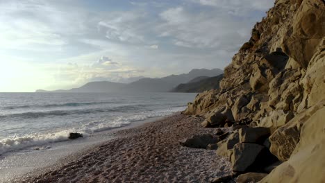 Dramatic-seascape-with-rocky-seaside-and-pebbles-beach-splashed-by-sea-waves-on-a-cloudy-day-in-Mediterranean