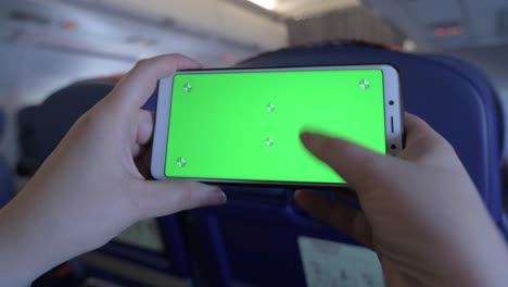 green screen on the screen of a mobile phone. chromakey smartphone. plays a game on a cell phone. gyroscope in a mobile device. phone in hands on board an airplane. leisure during a long flight.
