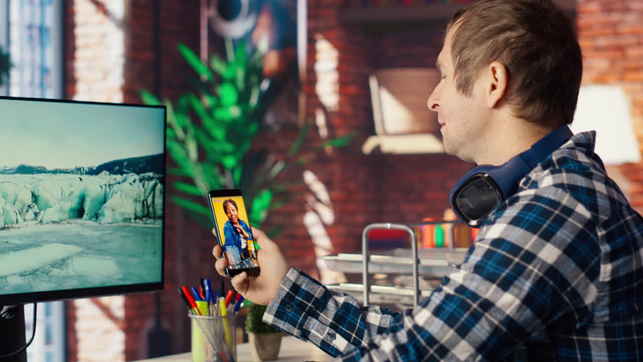 Man using phone, having PC monitor idle in front of him showing screensaver