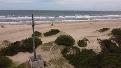 Toma-Aérea-De-La-Torre-De-Telecomunicaciones-Frente-A-La-Playa-De-Arena-Y-El-Océano-Atlántico-Durante-La-Luz-Del-Sol