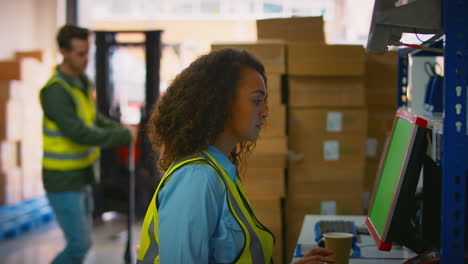 male and female workers using computer terminals and moving boxes in distribution warehouse