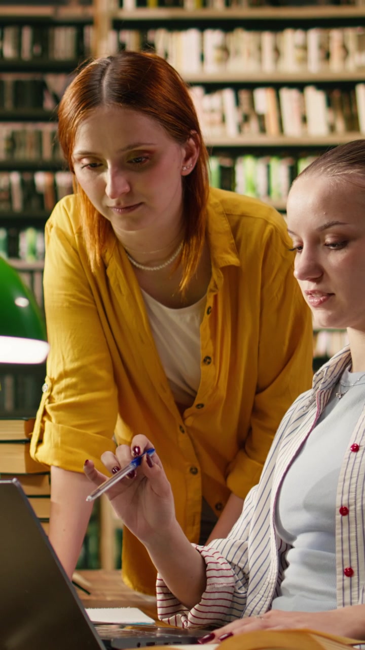 Vertikal video: Bibliotekveileder lener seg over bærbar PC for å hjelpe student med akademisk oppgave.