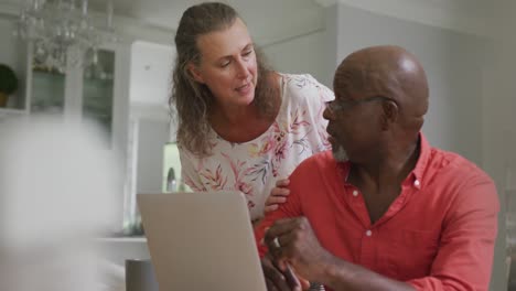 happy senior diverse couple wearing shirts and using laptop in living room