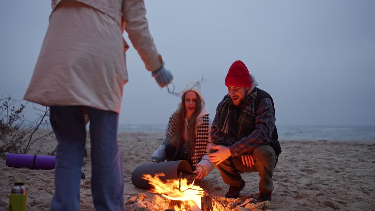 친구 들 이 밤 에 해변 에서 캠프 불 을 즐기고 있다