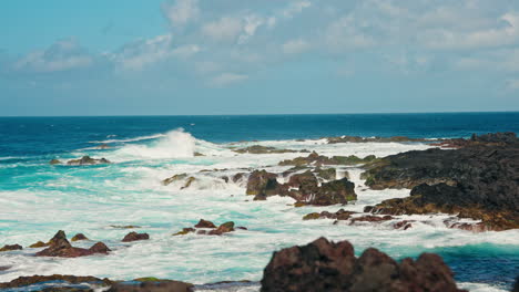 slow motion static close up shot of rough ocean waves crushing against the volcanic rocky coastline