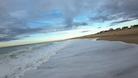 first person view drone flight over the waves at the wild surf beach of hossegor during a cloudy sunset