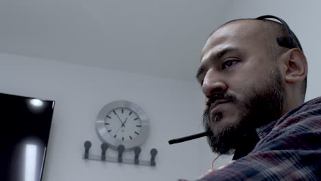 ethnic minority male wearing headset rocking back and forth in meeting room with wall clock in background