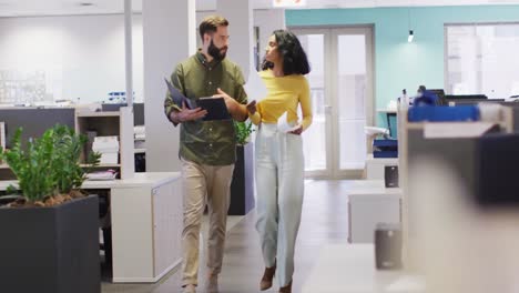 video of happy diverse businesswoman and businessman walking and talking in office