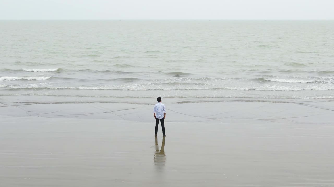 한 남자가 바 ⁇ 가에 혼자 서서 구름이 많은 날에 회색 지평선을 슬프거나 우울하게 쳐다보는 드론  ⁇ , 쿠아카타 바다, 방글라데시