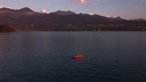 top down aerial view of a people paddling in a red paddling boat on the deep turquoise alpine lake thunersee in switzerland during sunset