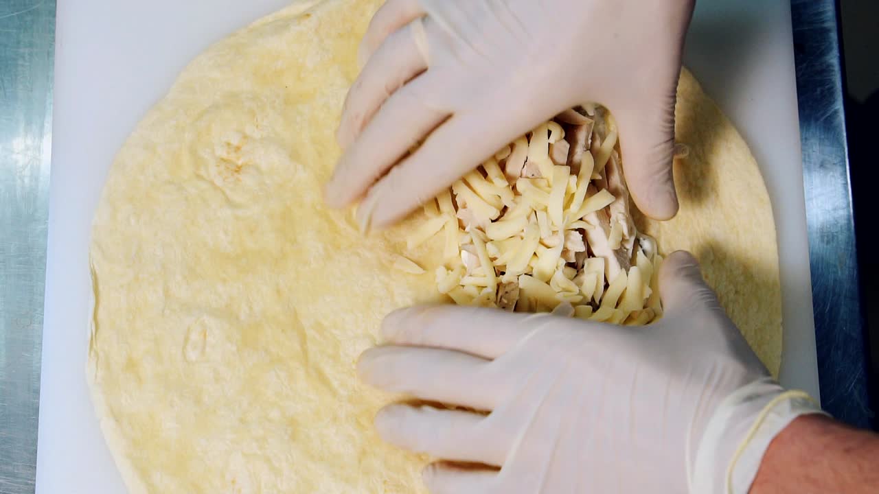 Cook is adding hard cheese on pita. Process of making delicious pita in the restaurant. Chef's hands in gloves cooking meat pita. Close-up