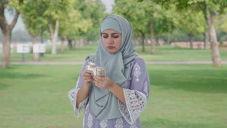 sad muslim woman counting money in park