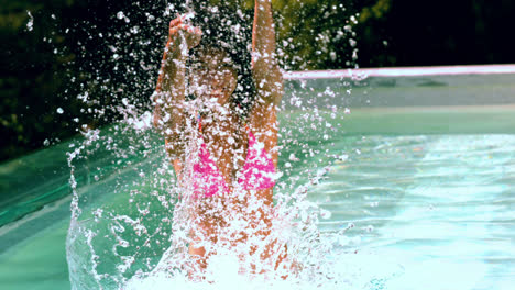 happy woman in pink bikini splashing at camera in swimming pool